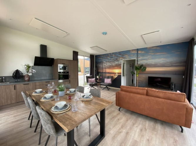 Interior de un lodge moderno con cocina abierta, mesa de comedor, sala y mural de atardecer en la pared.
