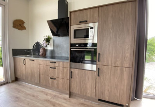 Moderne keukenkast in een lodge met houten kasten, inbouwoven, microgolf, zwart werkblad en decoratie.