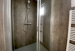 Moderne douchecabine bij een lodge met glazen deur, donkere wanden en een handdoekradiator.
