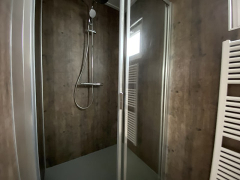 Moderna cabina de ducha en un lodge con puerta de vidrio, paredes oscuras y radiador toallero.