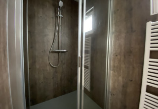 Cabine de douche moderne dans un lodge avec porte vitrée, murs foncés et sèche-serviettes blanc visible.