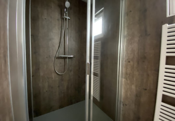 Modern shower cubicle at a lodge with glass door, dark wood-effect walls and towel radiator visible.