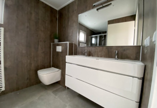 Salle de bain moderne dans un lodge avec toilette murale, double vasque et grand miroir au style minimaliste.