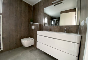 Moderne badeværelse i en lodge med væghængt toilet, dobbeltvask og stort spejl i minimalistisk stil.