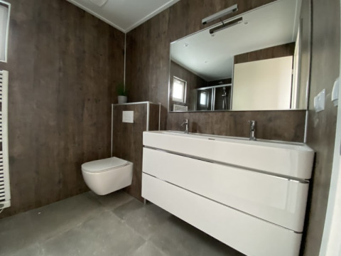 Baño moderno en una cabaña con inodoro suspendido, lavabo doble y espejo grande de estilo minimalista.
