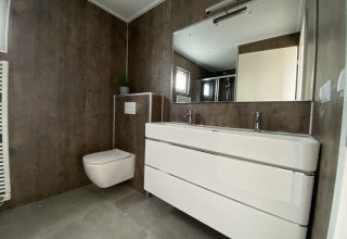 Moderne badkamer in een lodge met zwevend toilet, dubbele lavabo en grote spiegel in minimalistische stijl.