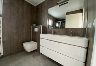Baño moderno en una cabaña con inodoro suspendido, lavabo doble y espejo grande de estilo minimalista.