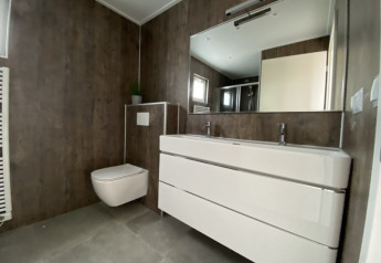 Moderne badeværelse i en lodge med væghængt toilet, dobbeltvask og stort spejl i minimalistisk stil.