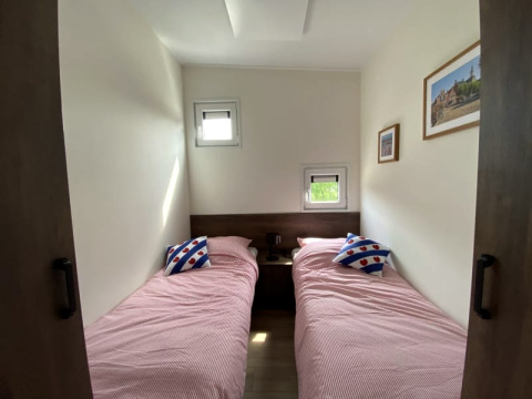 Photo d'une chambre de lodge avec deux lits simples, literie rose, coussins décoratifs et tableaux muraux.