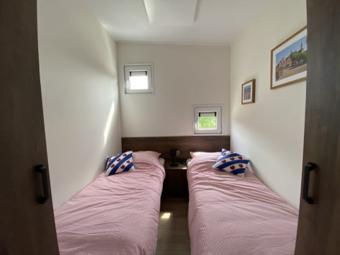Foto van een lodgekamer met twee aparte bedden, roze lakens, kussens en schilderijen aan de muur.