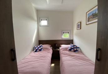 Photo d'une chambre de lodge avec deux lits simples, literie rose, coussins décoratifs et tableaux muraux.