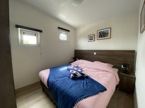 Foto van een gezellige slaapkamer in een lodge met een tweepersoonsbed, twee ramen en muurfoto's.