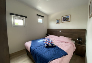 Foto van een gezellige slaapkamer in een lodge met een tweepersoonsbed, twee ramen en muurfoto's.