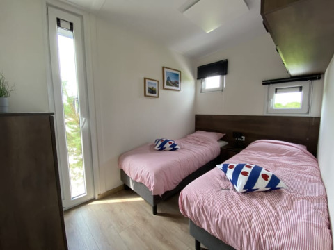 Habitación luminosa en una cabaña con dos camas individuales, ropa de cama a rayas y ventanas al exterior.