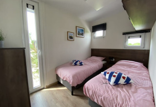Bright lodge room with two single beds, striped bedding, and windows showing greenery outside.