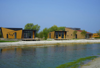 Cabañas modernas de madera junto a un lago, rodeadas de árboles y bajo un cielo azul durante el día.