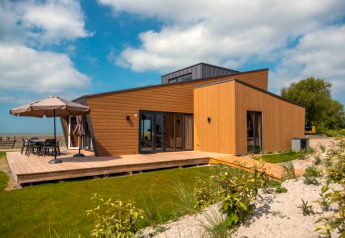 Moderne lodge met houten gevel, ruim terras en tuin, onder een licht bewolkte blauwe hemel.