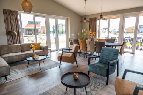 Espace salon-salle à manger d’une lodge moderne avec grandes baies vitrées et mobilier élégant, vue terrasse.