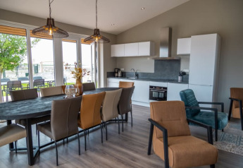 Interno di un lodge moderno con cucina a vista, tavolo da pranzo, poltrone e ampie finestre sul giardino.