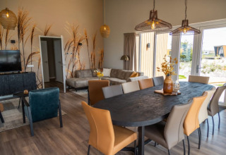 Intérieur de lodge moderne avec table à manger, chaises confortables, canapé, grandes fenêtres et mur végétal.