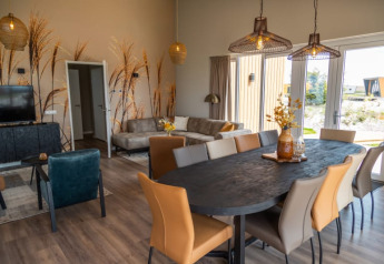 Interno di un lodge moderno con tavolo da pranzo, sedie comode, divano e grandi finestre decorate.