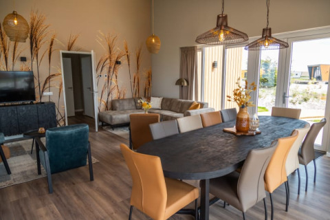 Intérieur de lodge moderne avec table à manger, chaises confortables, canapé, grandes fenêtres et mur végétal.