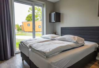 Dormitorio moderno en una cabaña con cama doble, ventanales grandes y vistas a zonas verdes exteriores.