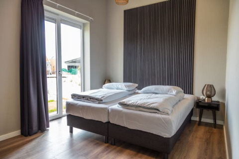 Moderne hotelværelse i en lodge med to enkeltsenge, store vinduer, træpanelvæg og natbord.