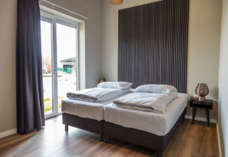 Chambre moderne dans un lodge avec deux lits simples, grandes fenêtres et un mur en bois stylisé.