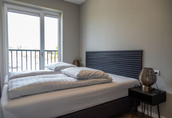 Camera moderna in un lodge con letto matrimoniale, grande finestra, testiera grigia ed elegante comodino.