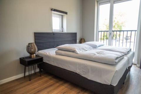 Chambre moderne de lodge avec lit double, tables de nuit, grande fenêtre et accès au balcon.