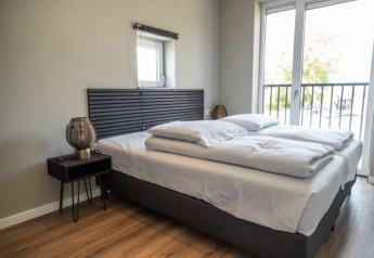 Moderne hotelværelse med dobbelt seng, natbord, vindue og balkon. Lyst rum med trægulv.
