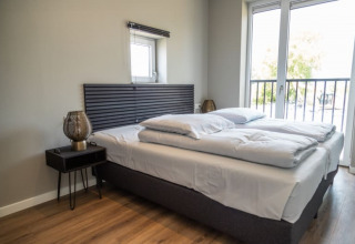 Chambre moderne de lodge avec lit double, tables de nuit, grande fenêtre et accès au balcon.
