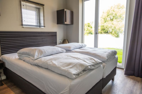 Dormitorio moderno de lodge con cama doble, ropa de cama blanca y puerta de cristal con vista al jardín.