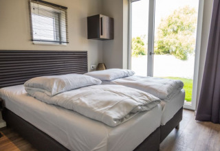 Dormitorio moderno de lodge con cama doble, ropa de cama blanca y puerta de cristal con vista al jardín.