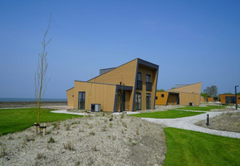 Lodge moderne con tetti inclinati, prati verdi e ambiente costiero sotto un cielo limpido e azzurro.