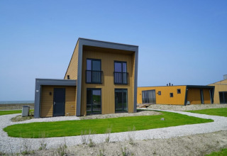 Moderna cabaña con techos planos y fachada de madera, ubicada en césped verde bajo un cielo azul claro.