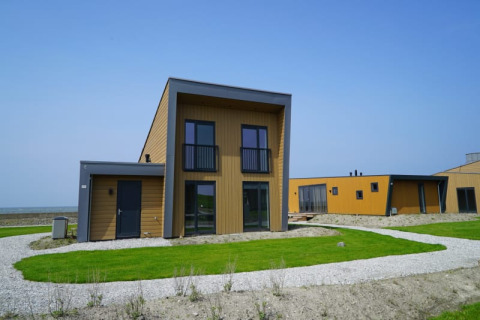 Moderna cabaña con techos planos y fachada de madera, ubicada en césped verde bajo un cielo azul claro.