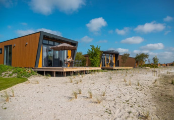 Moderne feriehytter med træfacader og store vinduer på sandet grund under blå himmel og solskin.