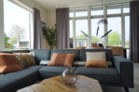 Moderne lodge woonkamer met veel licht, grijze zetel, decoratieve kussens en zicht op het groen.