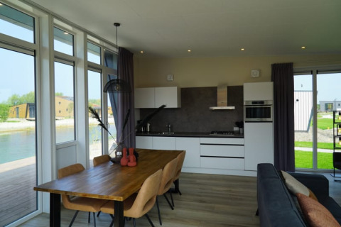 Lodge moderno con cocina abierta, mesa de madera y grandes ventanas con vista al agua y al exterior.