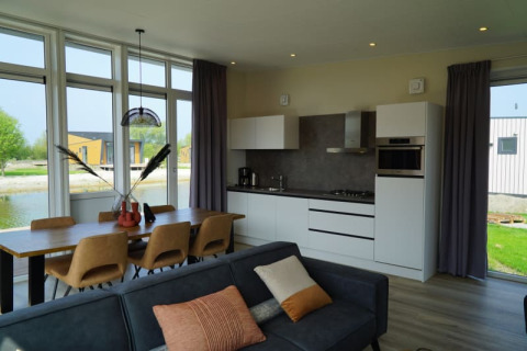 Lodge moderno con cocina abierta, mesa de comedor para seis, sofá y grandes ventanales con vistas al lago.