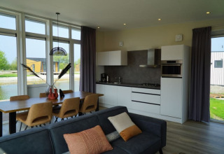 Lodge moderno con cocina abierta, mesa de comedor para seis, sofá y grandes ventanales con vistas al lago.