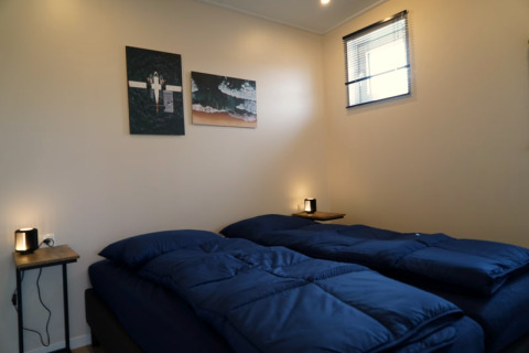 Gezellige lodgekamer met twee eenpersoonsbedden, donkerblauw beddengoed, wanddecoratie en klein raam.