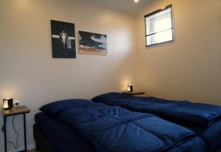 Gezellige lodgekamer met twee eenpersoonsbedden, donkerblauw beddengoed, wanddecoratie en klein raam.