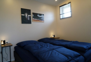 Habitación acogedora en una cabaña con dos camas individuales, ropa de cama azul oscuro y arte en la pared.