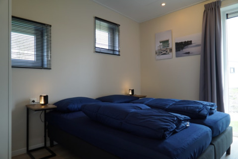 Dormitorio moderno en una cabaña, con dos camas individuales, ropa de cama azul y lámparas en las mesas.