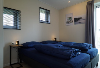 Dormitorio moderno en una cabaña, con dos camas individuales, ropa de cama azul y lámparas en las mesas.