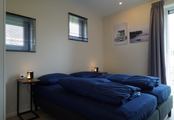 Chambre moderne d'un lodge avec deux lits simples, literie bleue et lampes sur des tables de chevet.