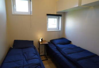 Small lodge room with two single beds, blue bedding and a small table with a lamp placed in between.